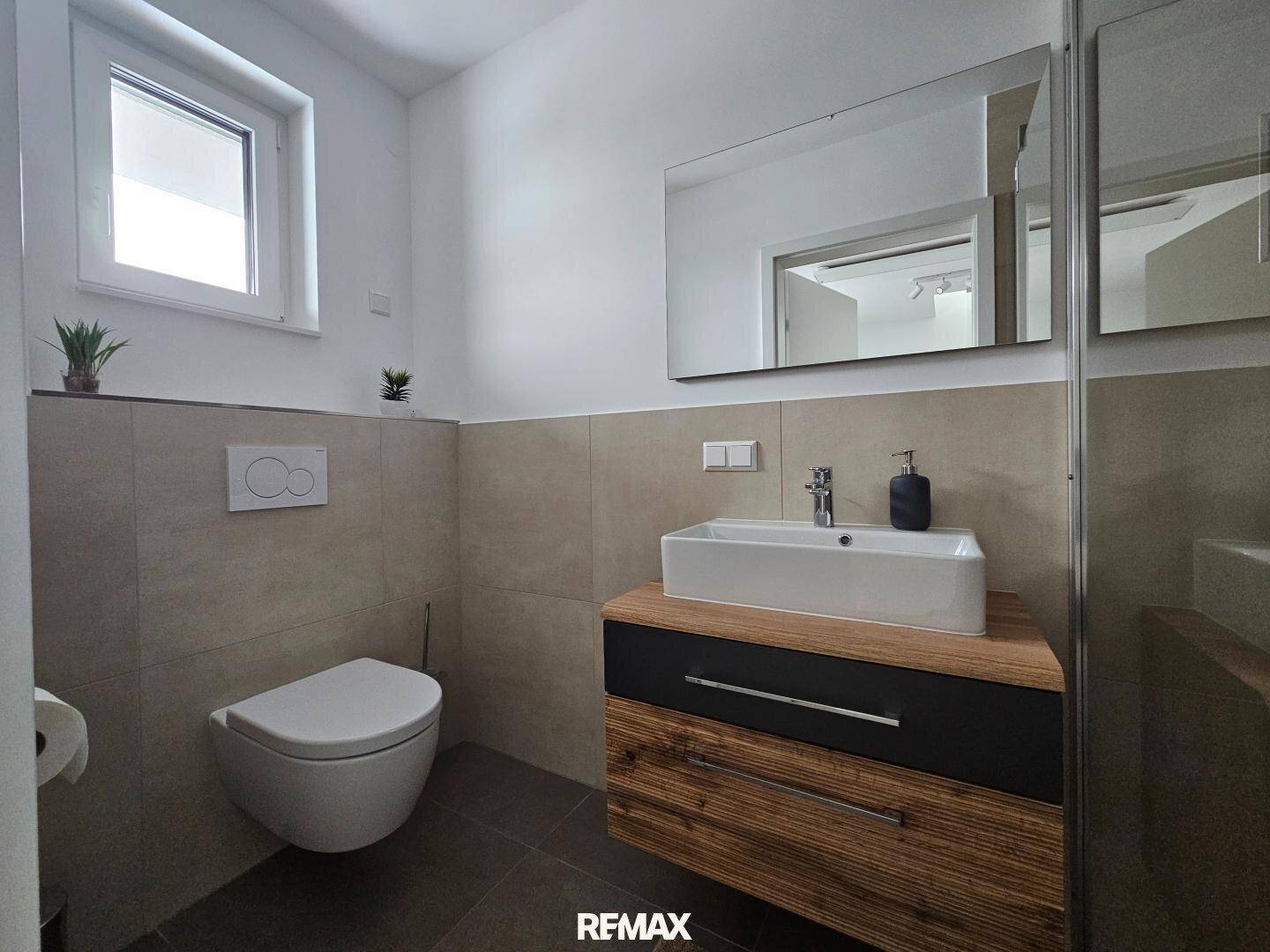Modernes Gäste-WC mit Wand-WC, Waschbecken und Fenster für Tageslicht.