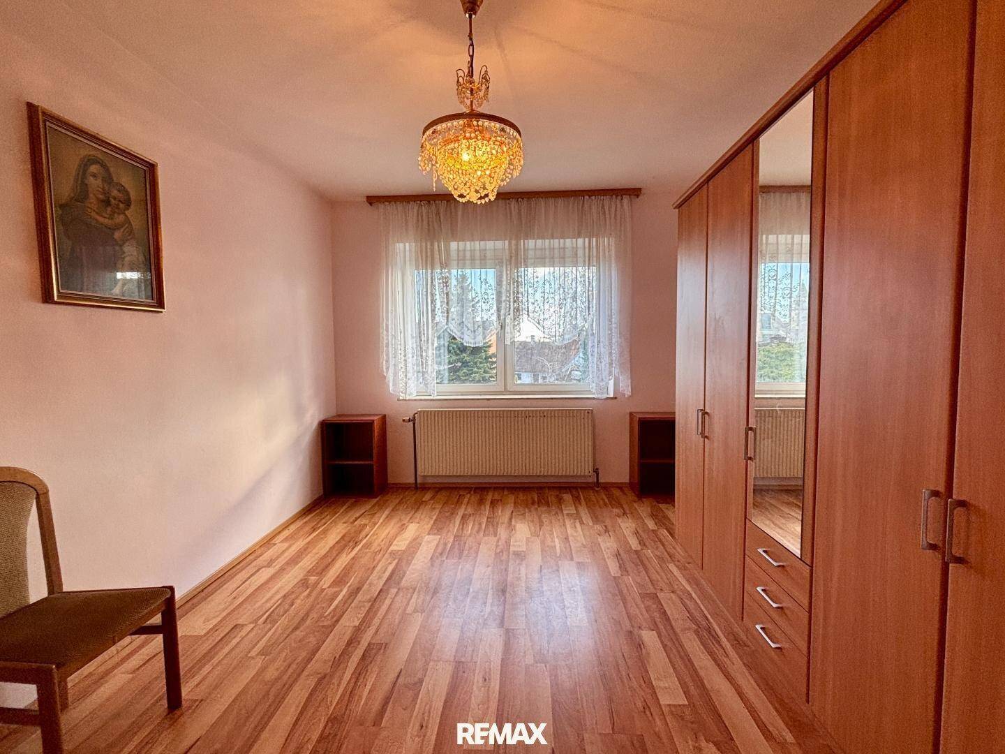 Helles Schlafzimmer mit Holzboden, großem Kleiderschrank und Fensterblick.