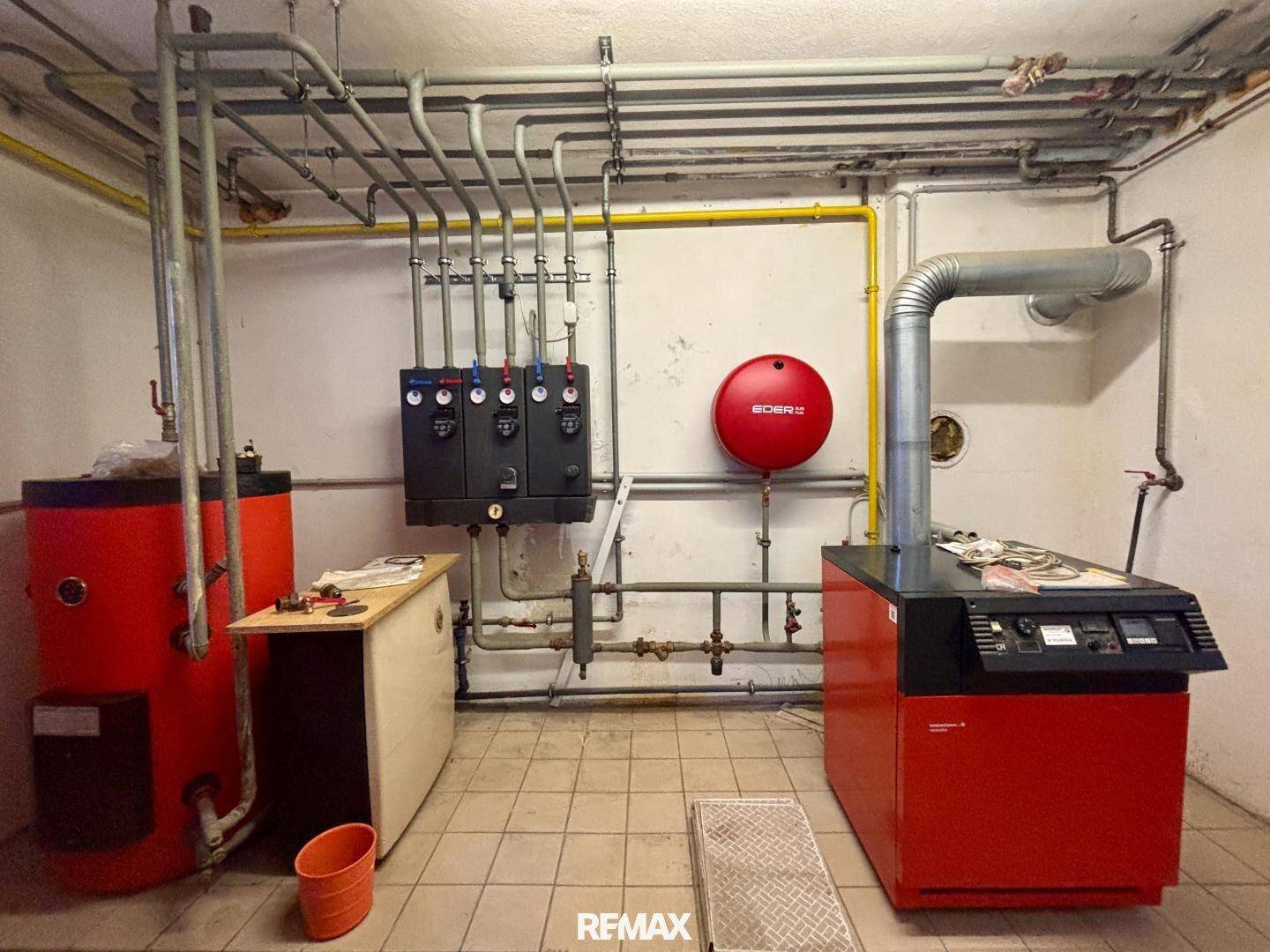 Heizungsraum im Keller mit Kessel, Warmwasserspeicher und sichtbaren Rohren.