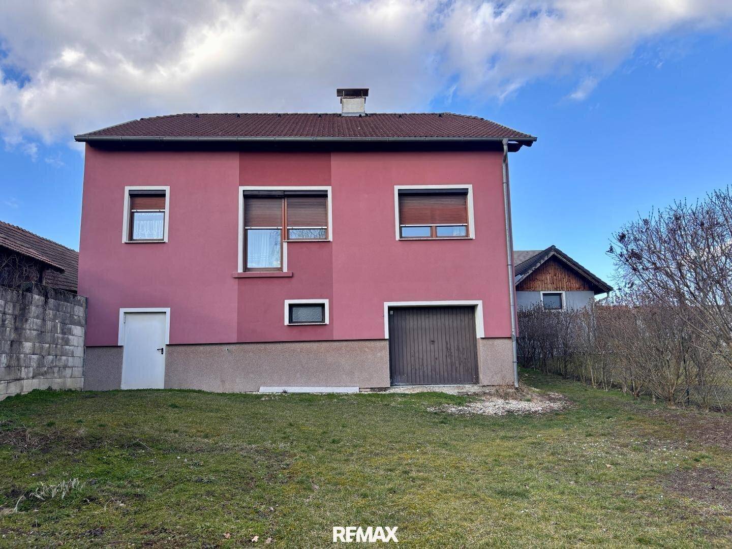 Rückseite des Hauses mit Garage und Gartenbereich unter bewölktem Himmel.