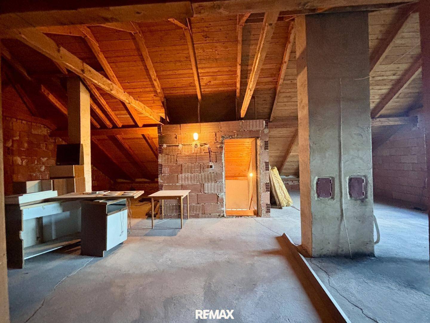 Unausgebauter Dachboden mit sichtbaren Holzbalken und Ziegelwänden, bietet Ausbaupotenzial.