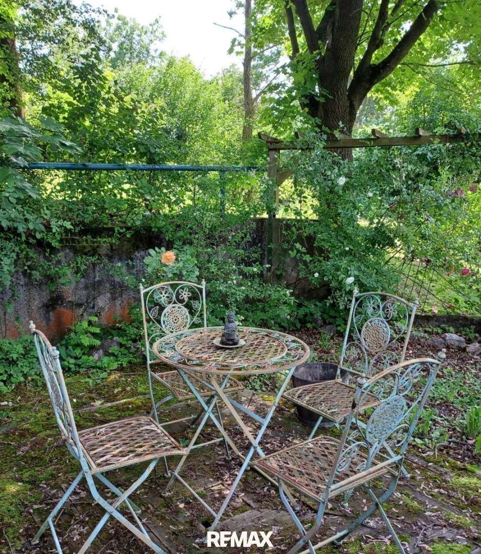 Romantische Sitzecke im Garten mit schmiedeeisernen Möbeln und üppiger Vegetation.