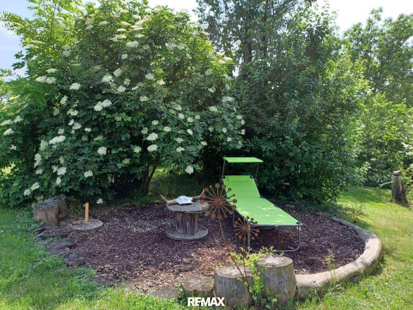 Gemütlicher Liegebereich im Garten mit Liegestuhl und blühenden Sträuchern.