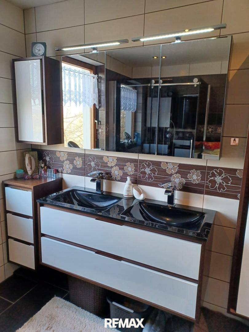 Modernes Badezimmer mit Doppelwaschbecken, Spiegelschrank und floralen Akzentfliesen.