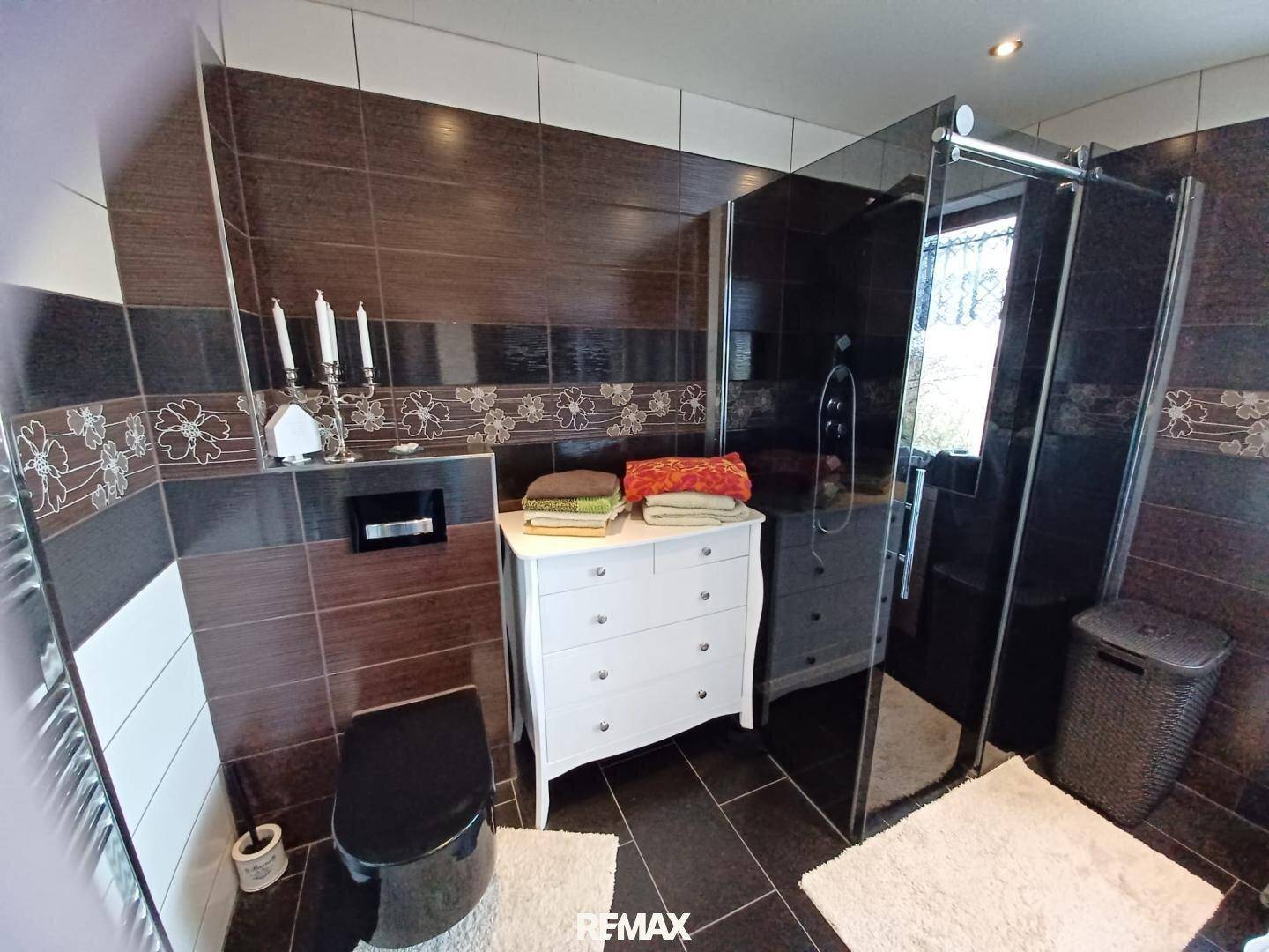 Elegantes Badezimmer mit dunklen Fliesen, begehbarer Dusche und wandhängendem WC.