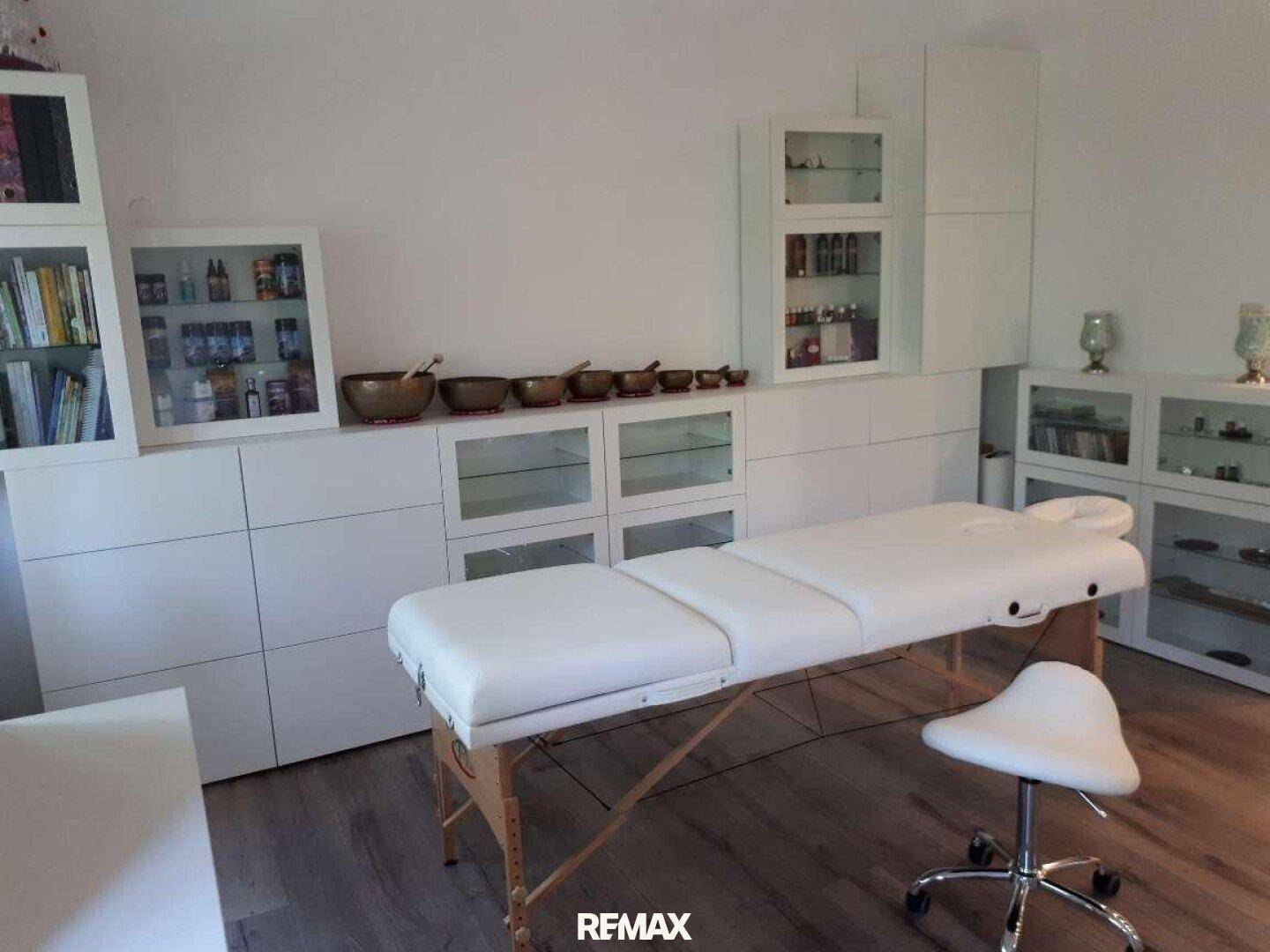 Helles Zimmer mit Massageliege und weißen Schränken, ideal für eine Praxis oder ein Büro.
