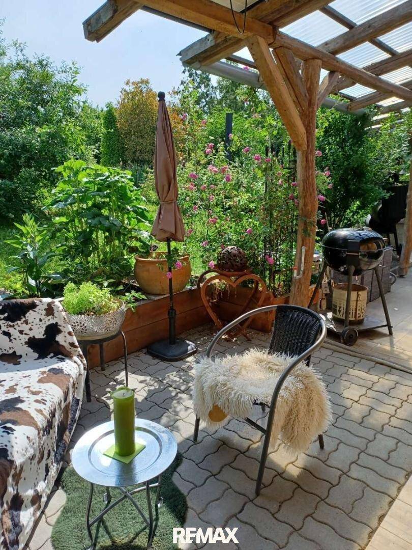 Sonnige Terrasse mit Sitzgelegenheiten, Grillplatz und üppiger Bepflanzung im Garten.