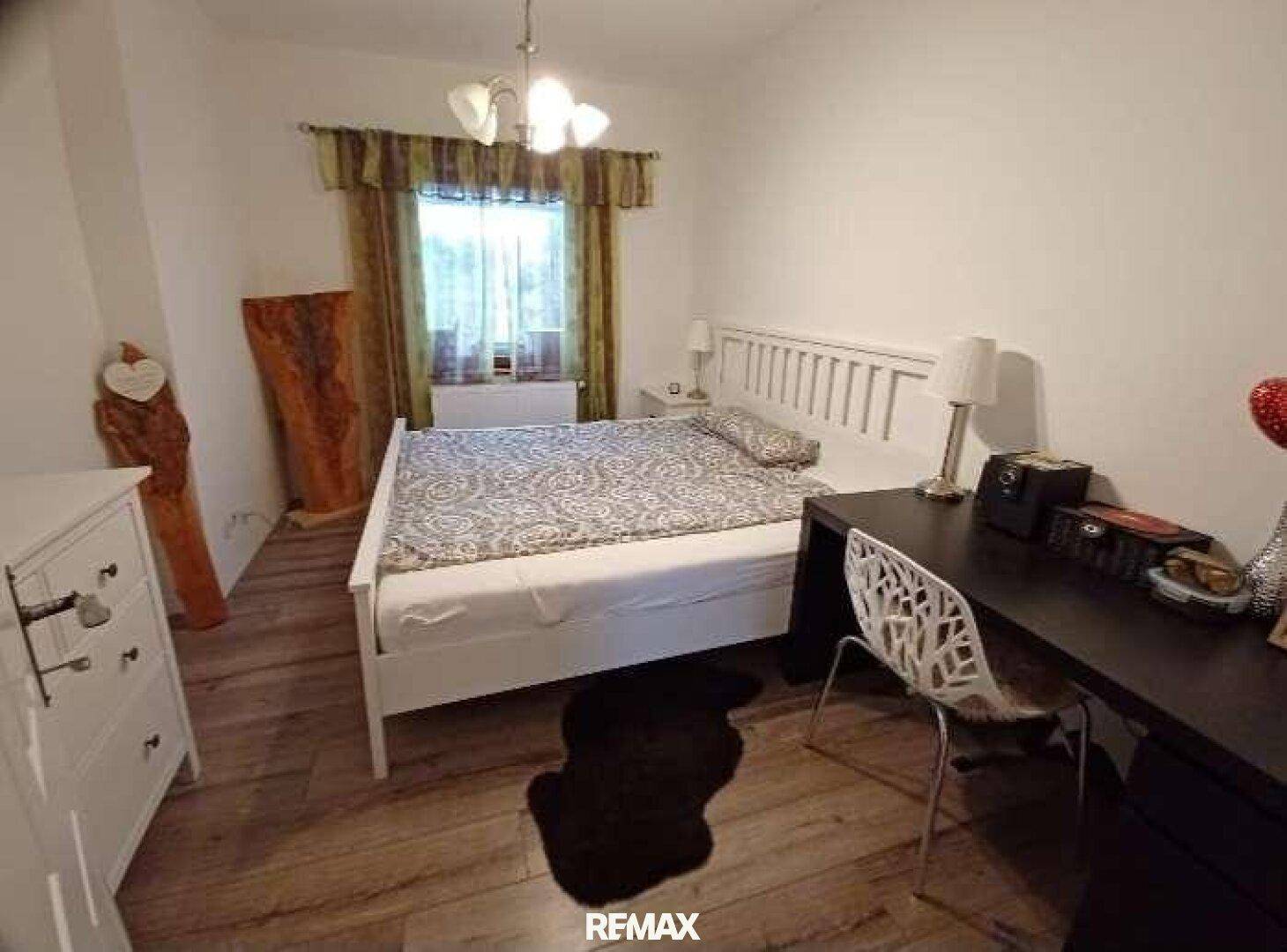 Gemütliches Schlafzimmer mit Holzboden, Doppelbett und einem Schreibtisch am Fenster.