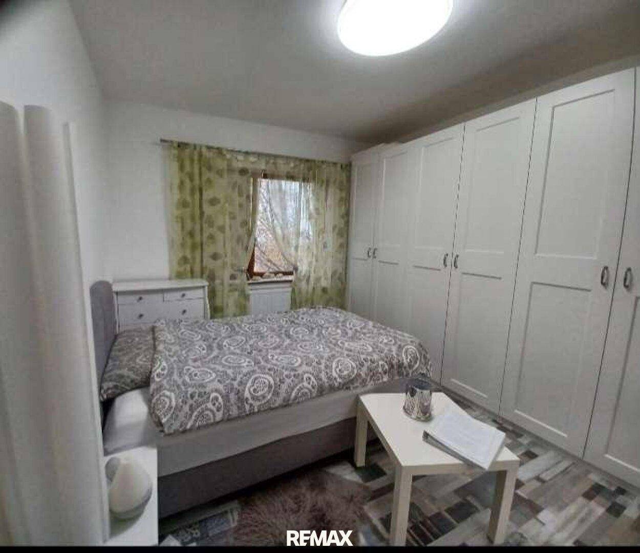 Helles Schlafzimmer mit großem Kleiderschrank, Doppelbett und gemusterten Vorhängen.