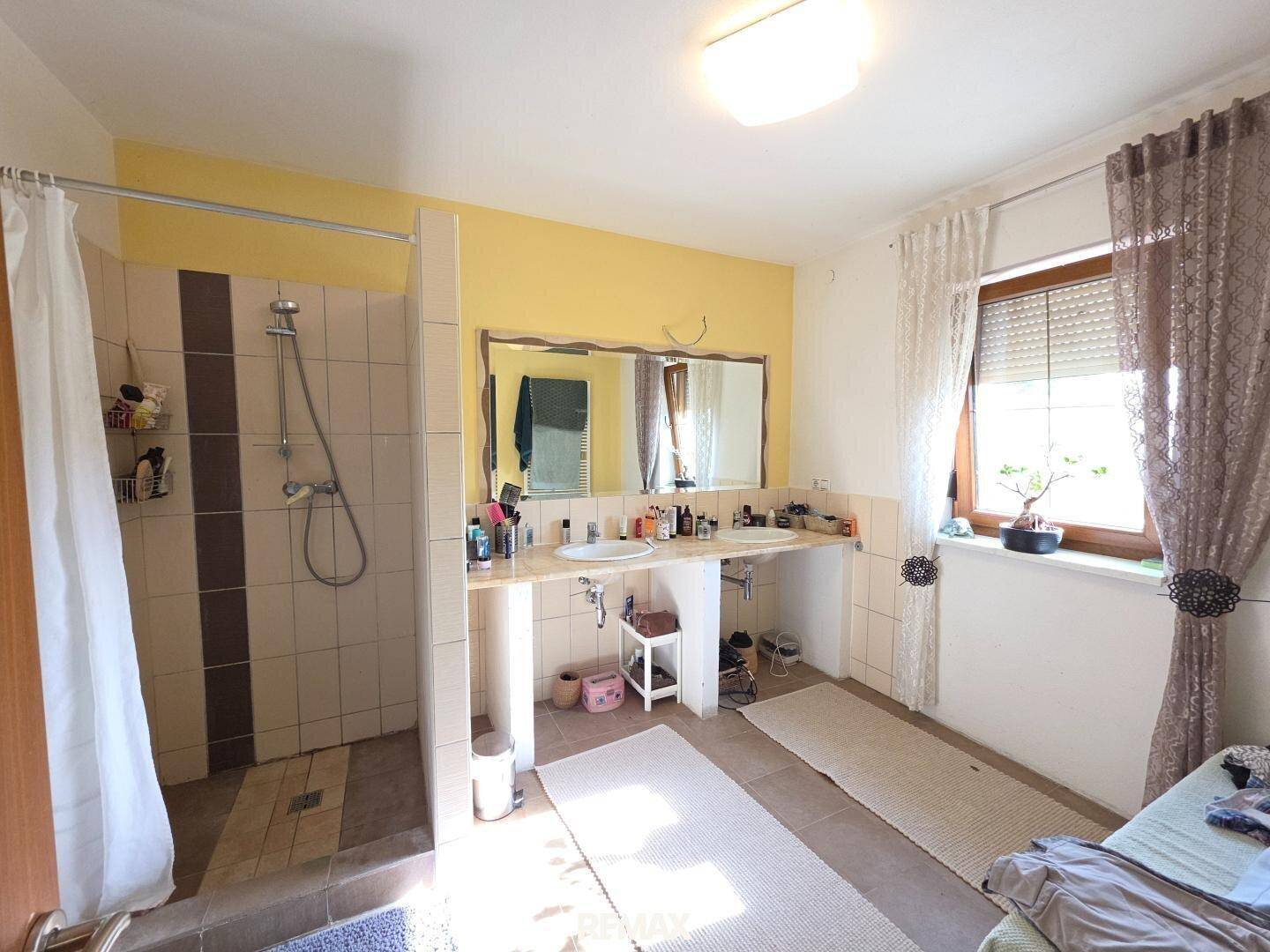 Geräumiges Badezimmer mit Doppelwaschbecken, großer Duschkabine und Fenster.