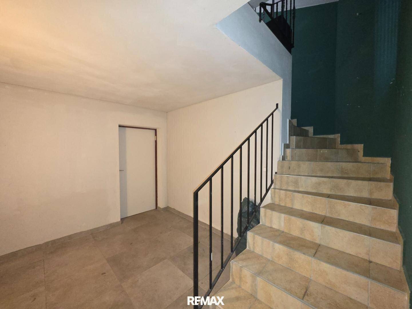 Treppenabgang in den Keller mit gefliestem Boden und schlichten weißen Wänden.