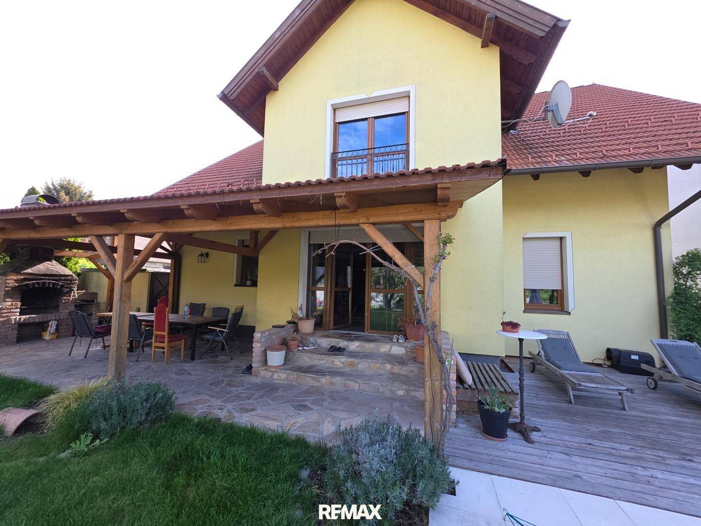 Überdachte Steinterrasse mit Holzpergola, Sonnenliegen und direktem Zugang zum Garten und Pool.