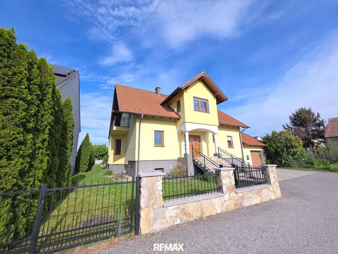 Freistehendes Einfamilienhaus mit gelber Fassade, rotem Ziegeldach und gepflegtem Vorgarten.