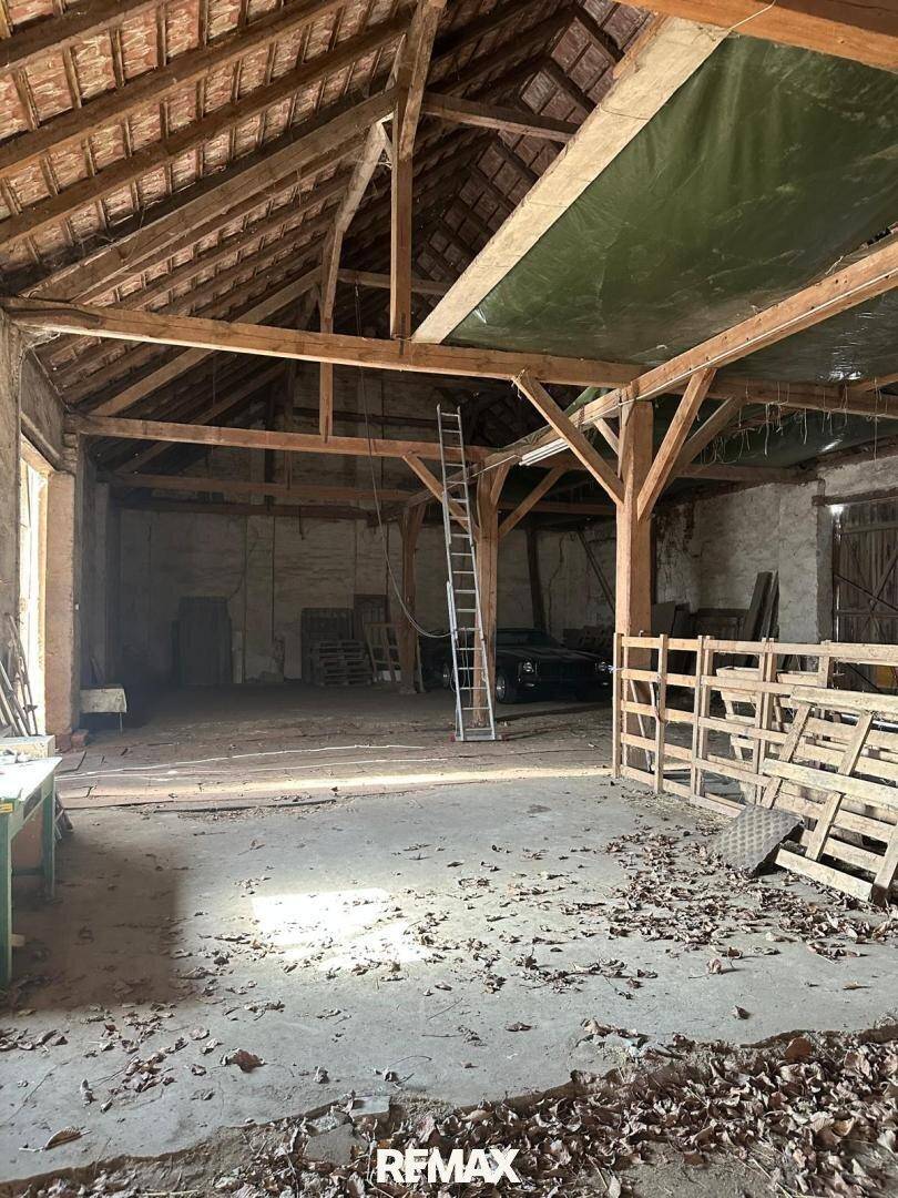 Großer, leerer Scheunenraum mit beeindruckender Holzkonstruktion und viel natürlichem Licht.