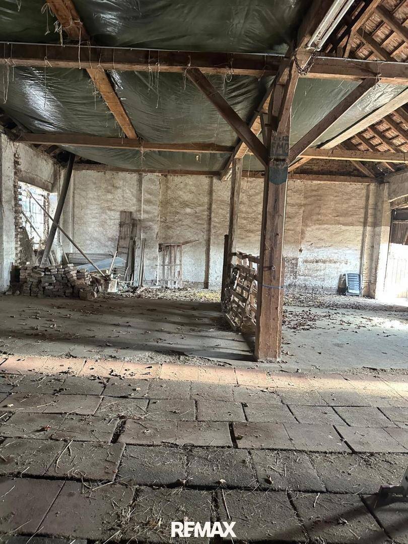 Geräumiger, leerstehender Innenraum mit sichtbarer Holzkonstruktion und alten Fliesen.