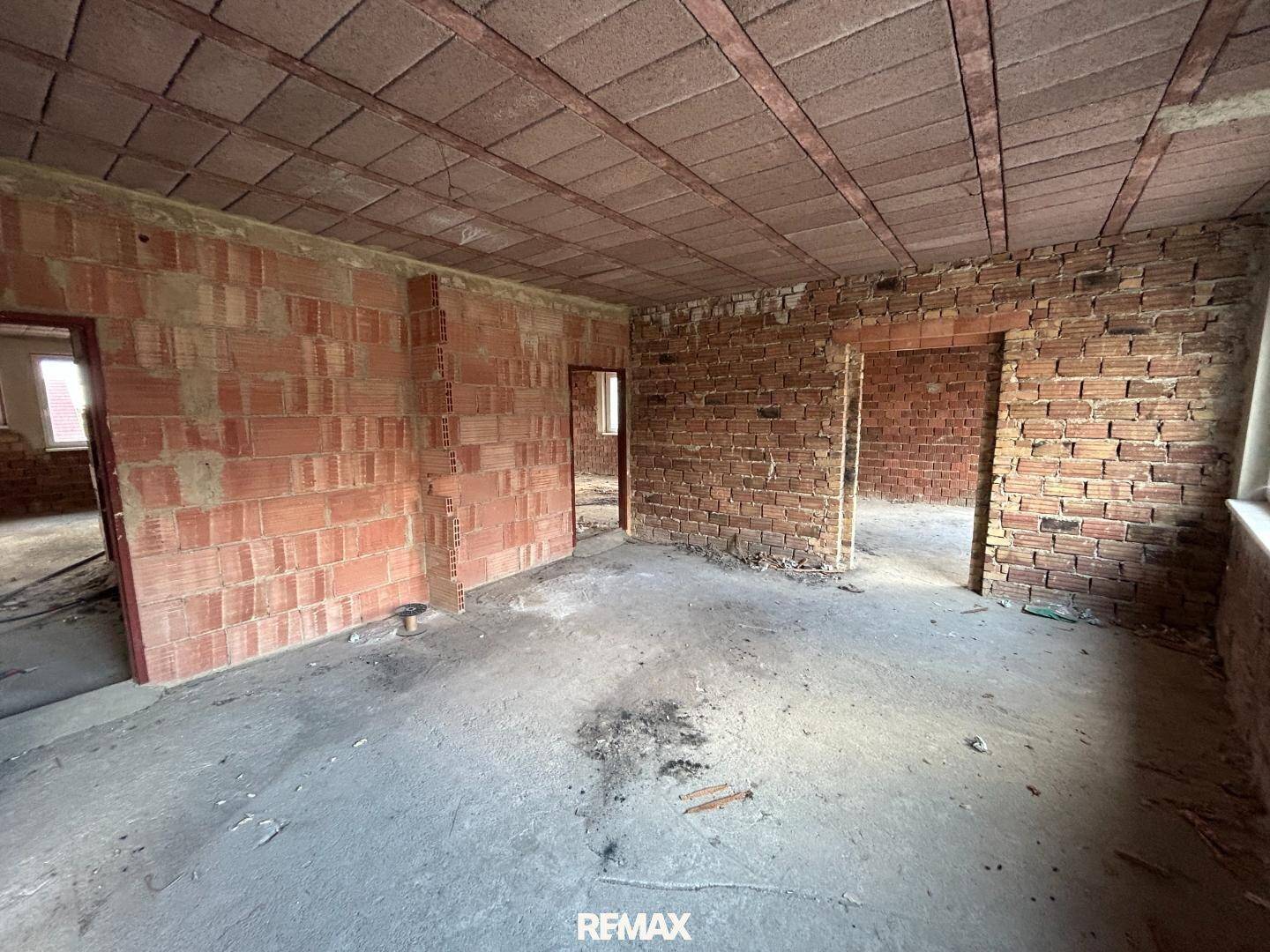 Rohbauzimmer mit unverputzten Ziegelwänden, Betonboden und Türöffnungen, bereit für den Ausbau.