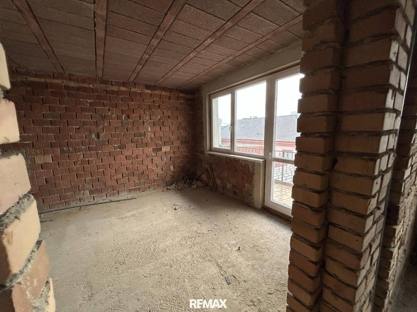 Rohbauzimmer mit unverputzten Ziegelwänden, Betonboden und einer Tür zum Balkon oder zur Terrasse.