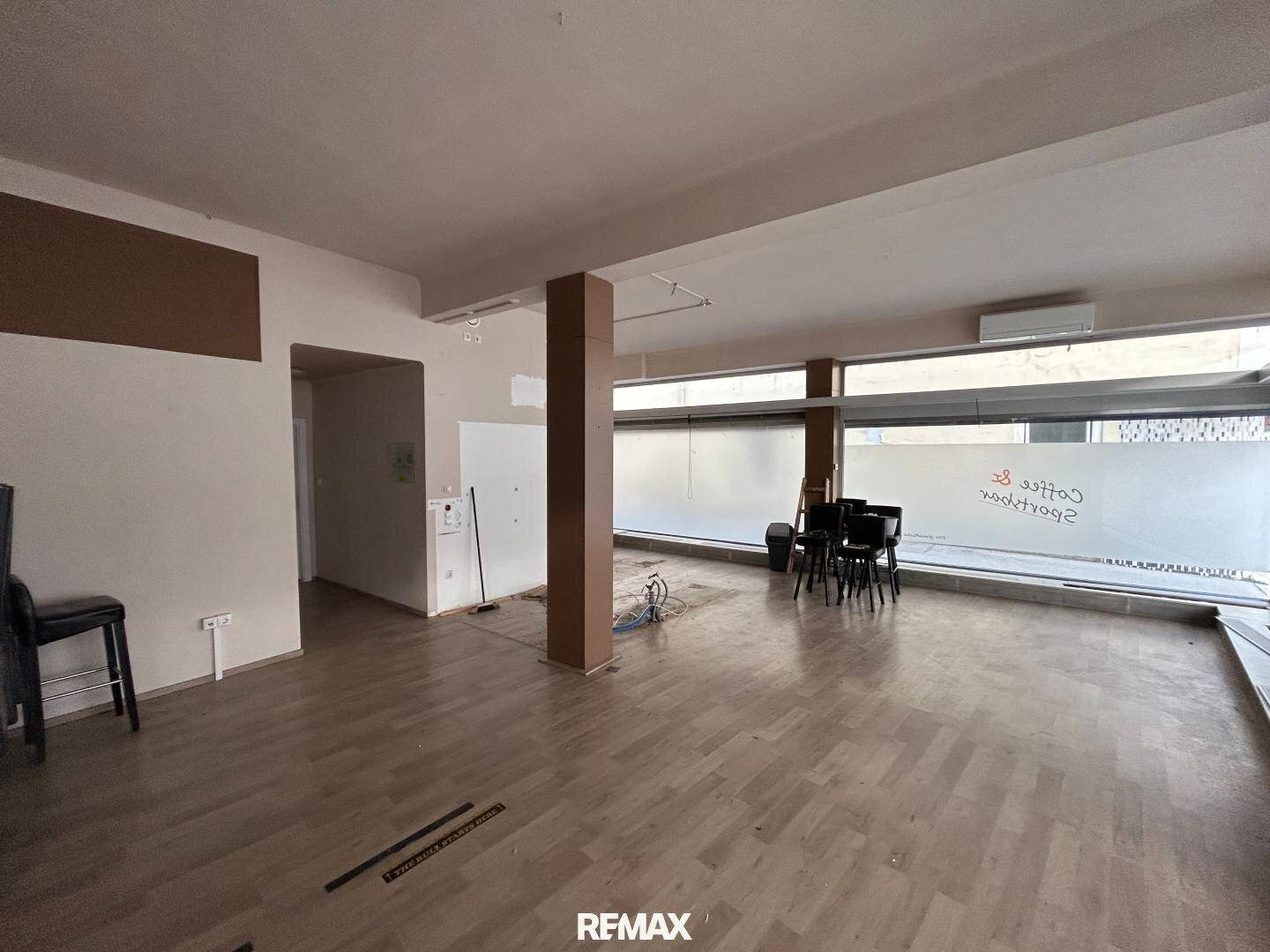 Großer, leerer Gewerberaum mit Holzboden, breiter Fensterfront und sichtbaren Installationsarbeiten.