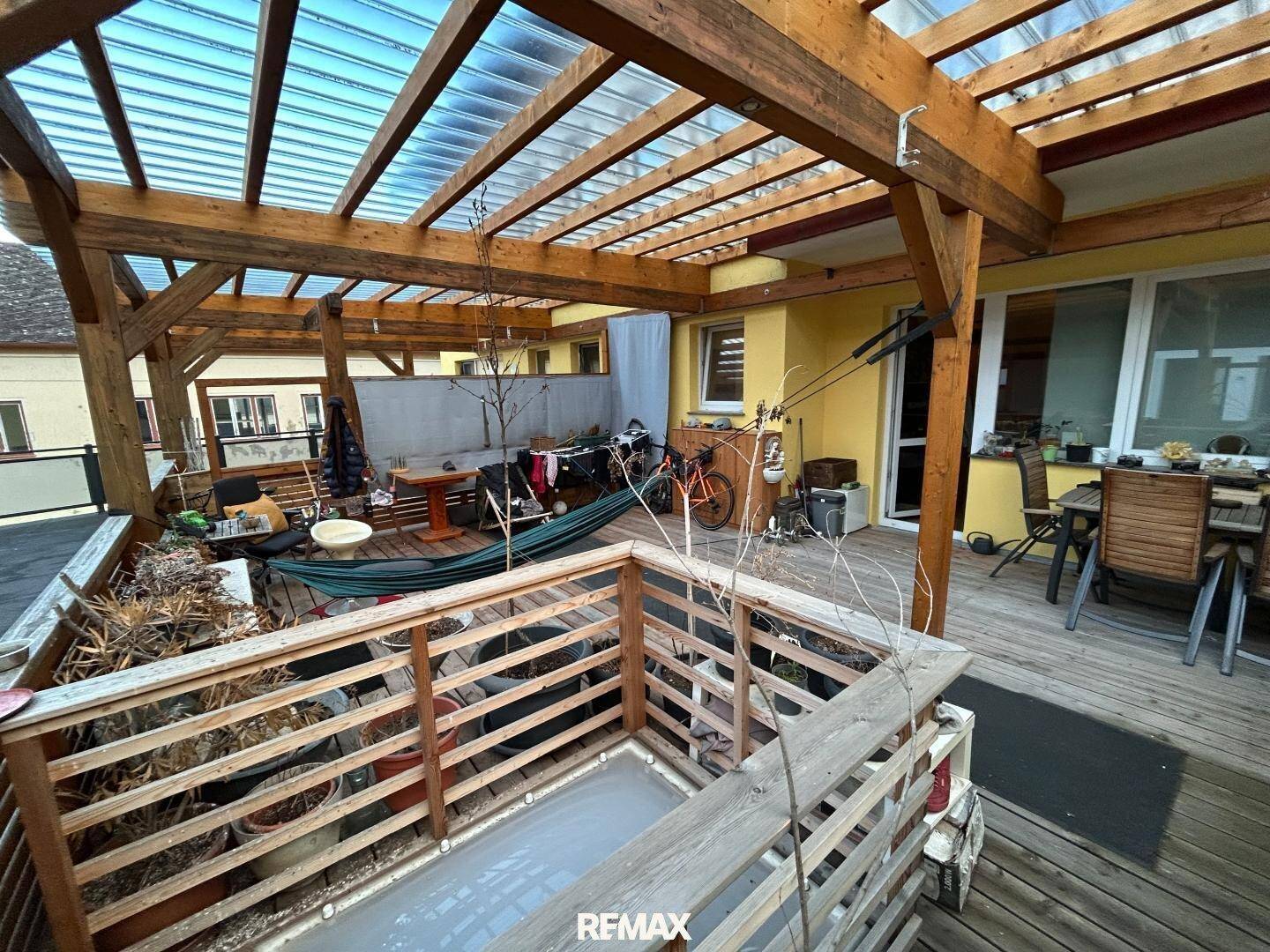 Große Dachterrasse mit Holzpergola, Sitzgelegenheiten und einem kleinen bepflanzten Bereich.