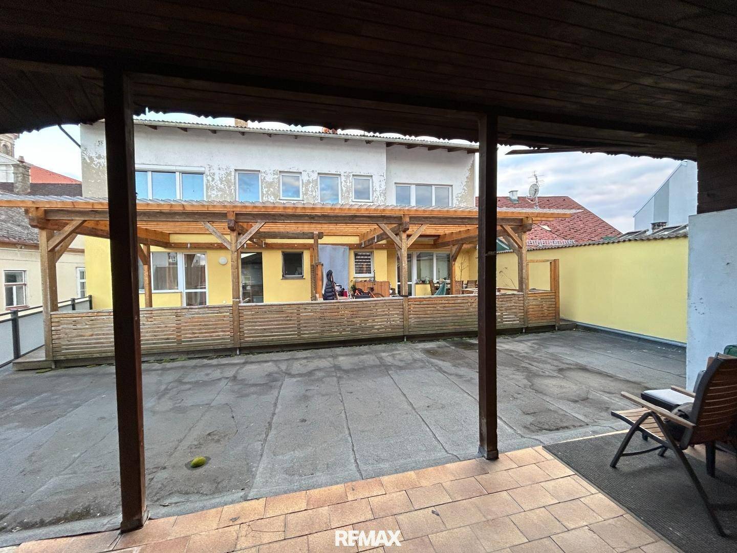 Großer Außenbereich mit überdachter Terrasse, Holzzaun und Blick auf das Gebäude.