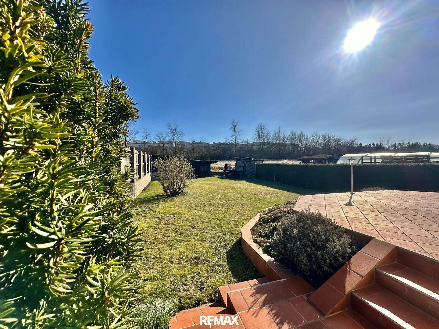 Großer, sonniger Garten mit Rasenfläche, Hecke und Blick ins Grüne.