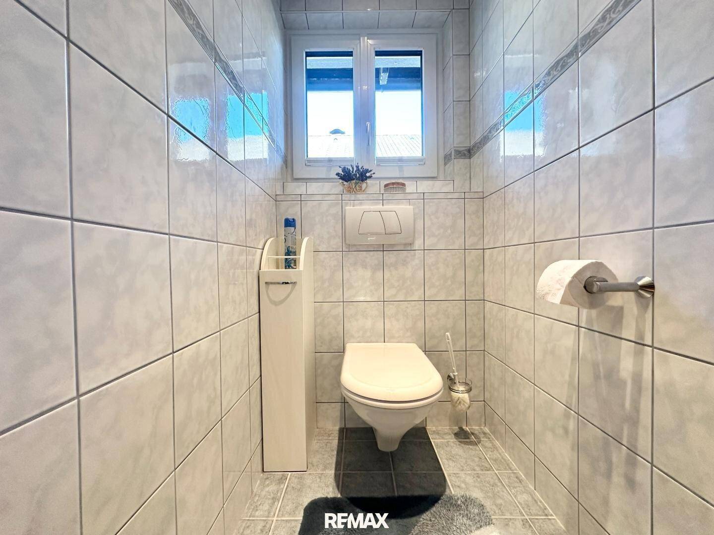 Separates WC mit Wandfliesen, Fenster und wandhängendem WC.