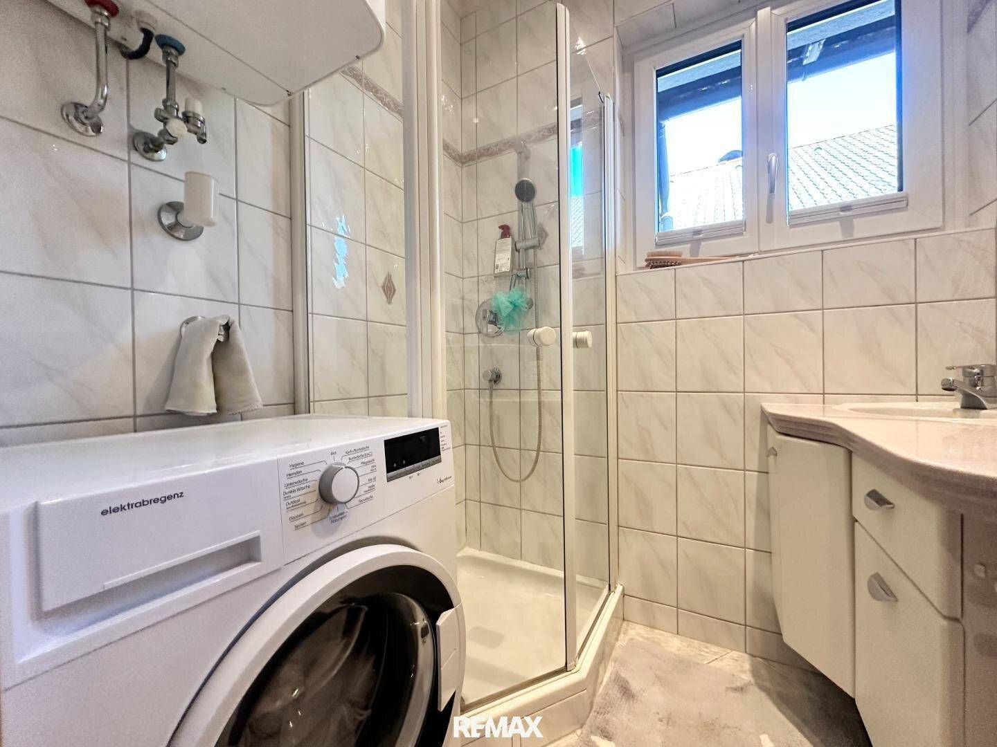 Gefliestes Badezimmer mit Duschkabine, Waschbecken und integrierter Waschmaschine.