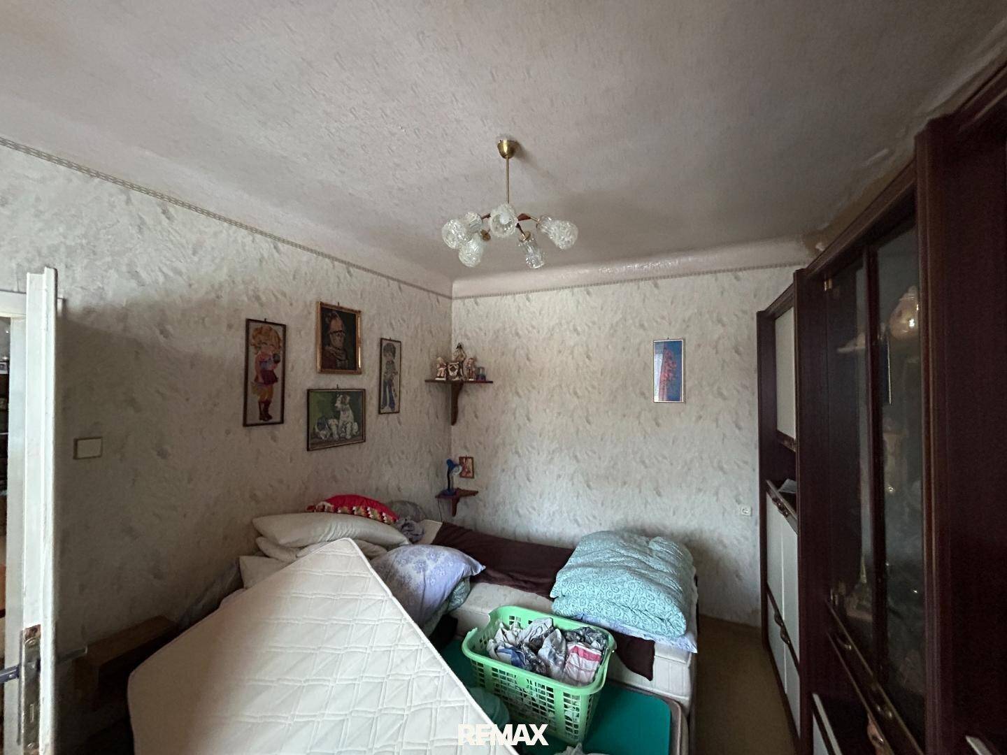Schlafzimmer mit einfacher Einrichtung, gemusterter Tapete und einem Kleiderschrank.