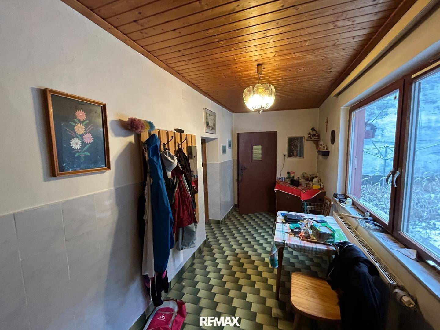 Flur mit Holzdecke, Garderobe und Blick auf den Außenbereich durch große Fenster.