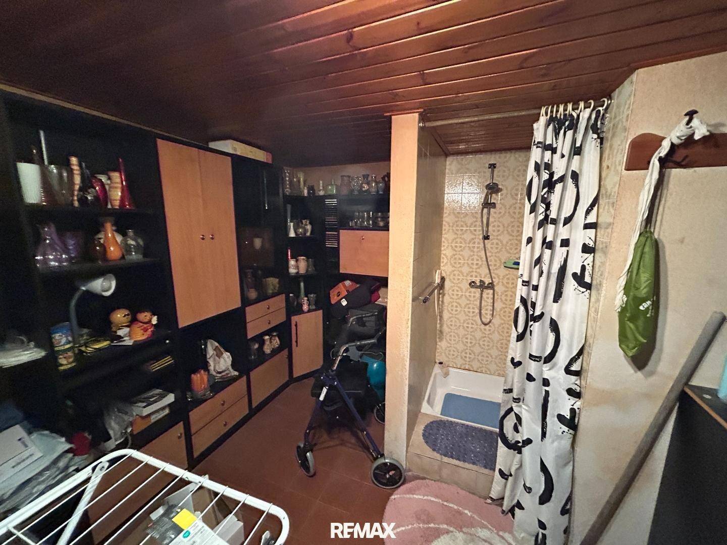 Abstellraum mit Holzdecke, Regalen und einer einfachen Duschkabine.