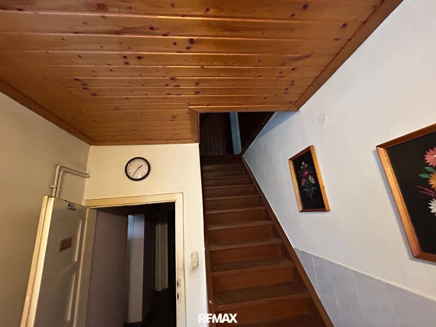 Treppenhaus mit Holztreppe, Holzdecke und Uhr an der Wand.