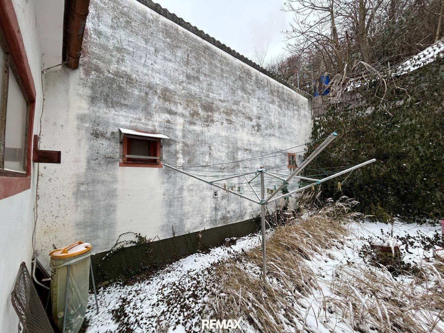 Rückseite eines Gebäudes mit Wäscheständer und schneebedecktem, verwildertem Gartenbereich.