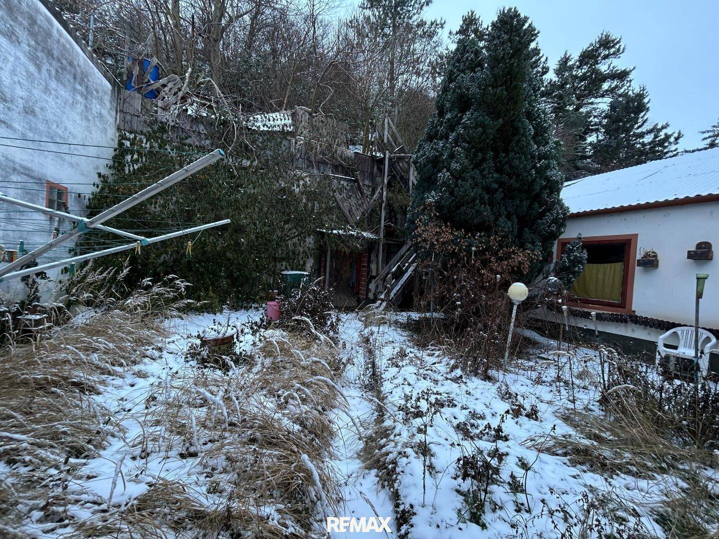 Winterlicher Gartenbereich mit Schnee, Bäumen und einem Wäscheständer.