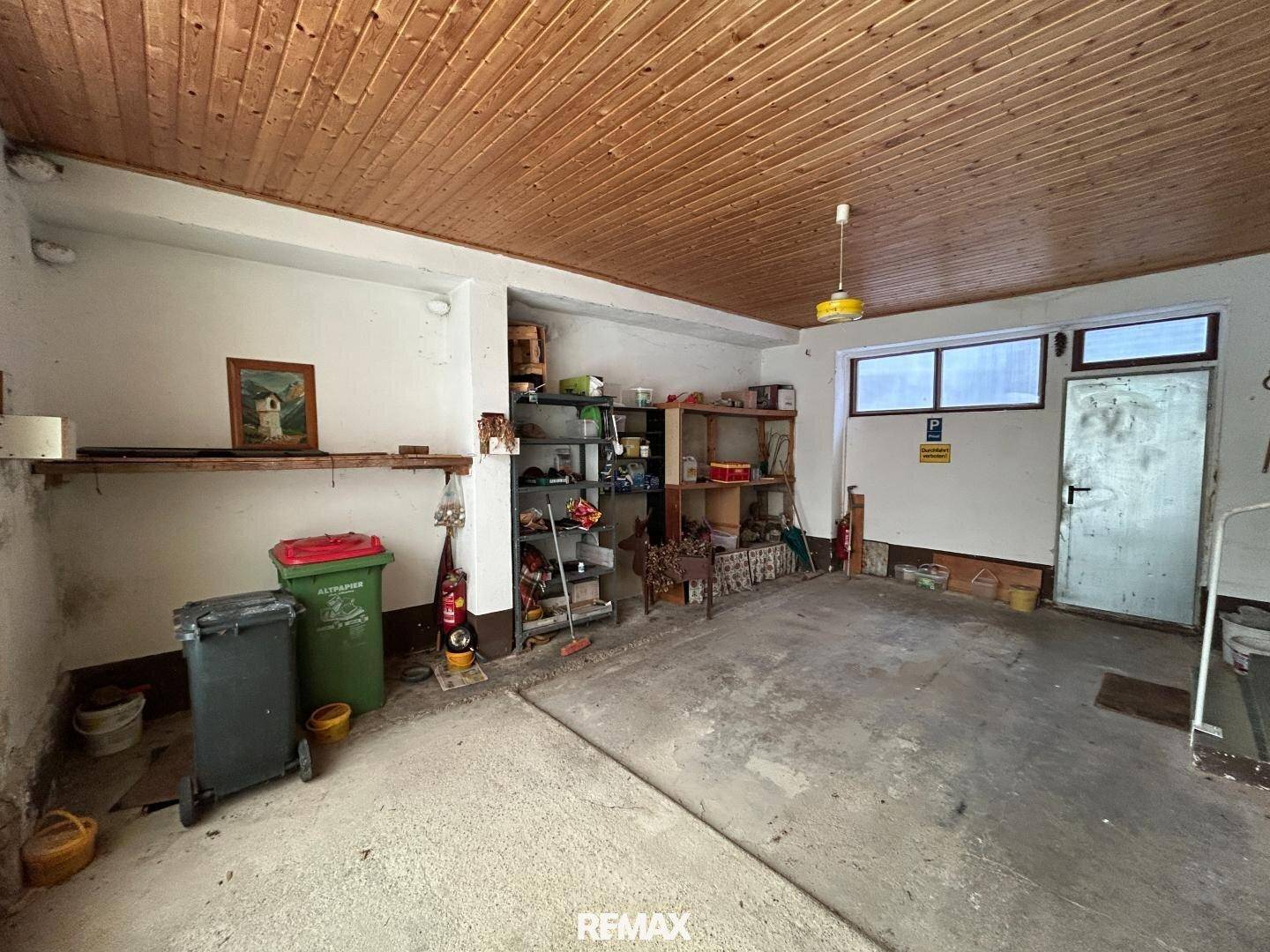 Geräumige Garage mit Betonboden, Holzdecke und Regalen für Lagerung.