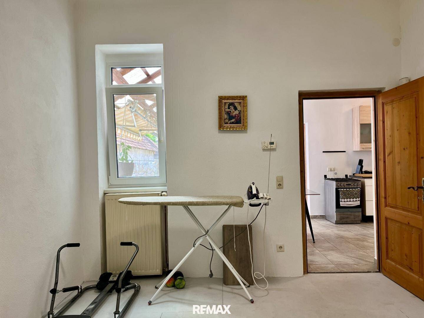 Einfacher Raum mit Bügelbrett und Fenster, angrenzend an die Küche, ideal als Hauswirtschaftsraum.