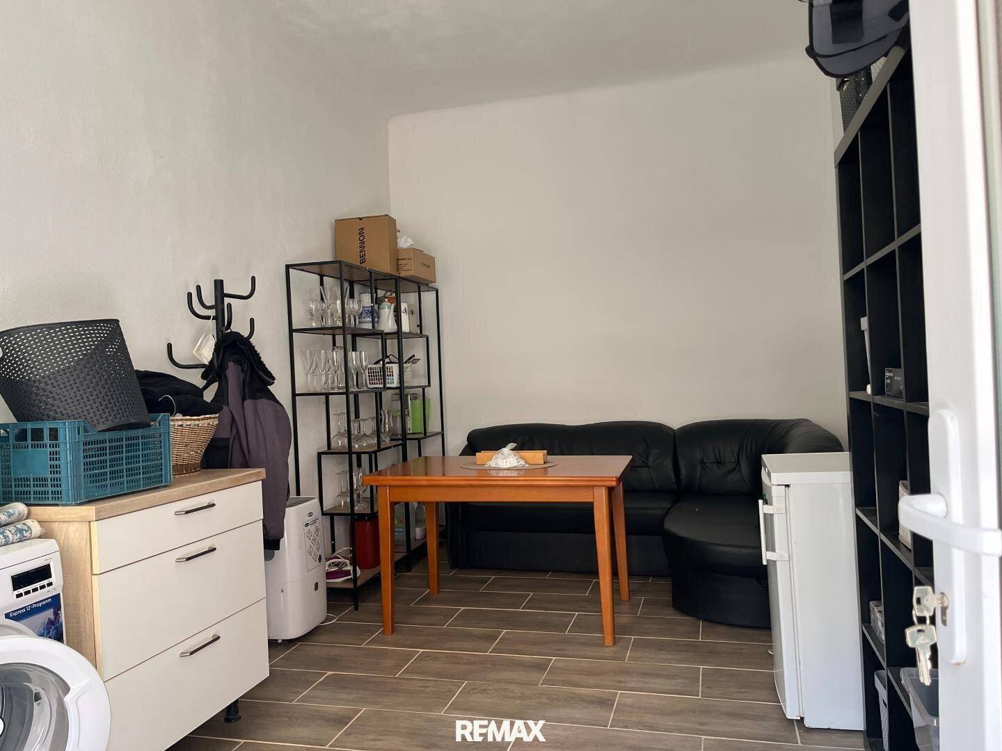 Einfacher Wohnbereich mit Sofa, Tisch und Regalen, auch als Abstellraum genutzt.