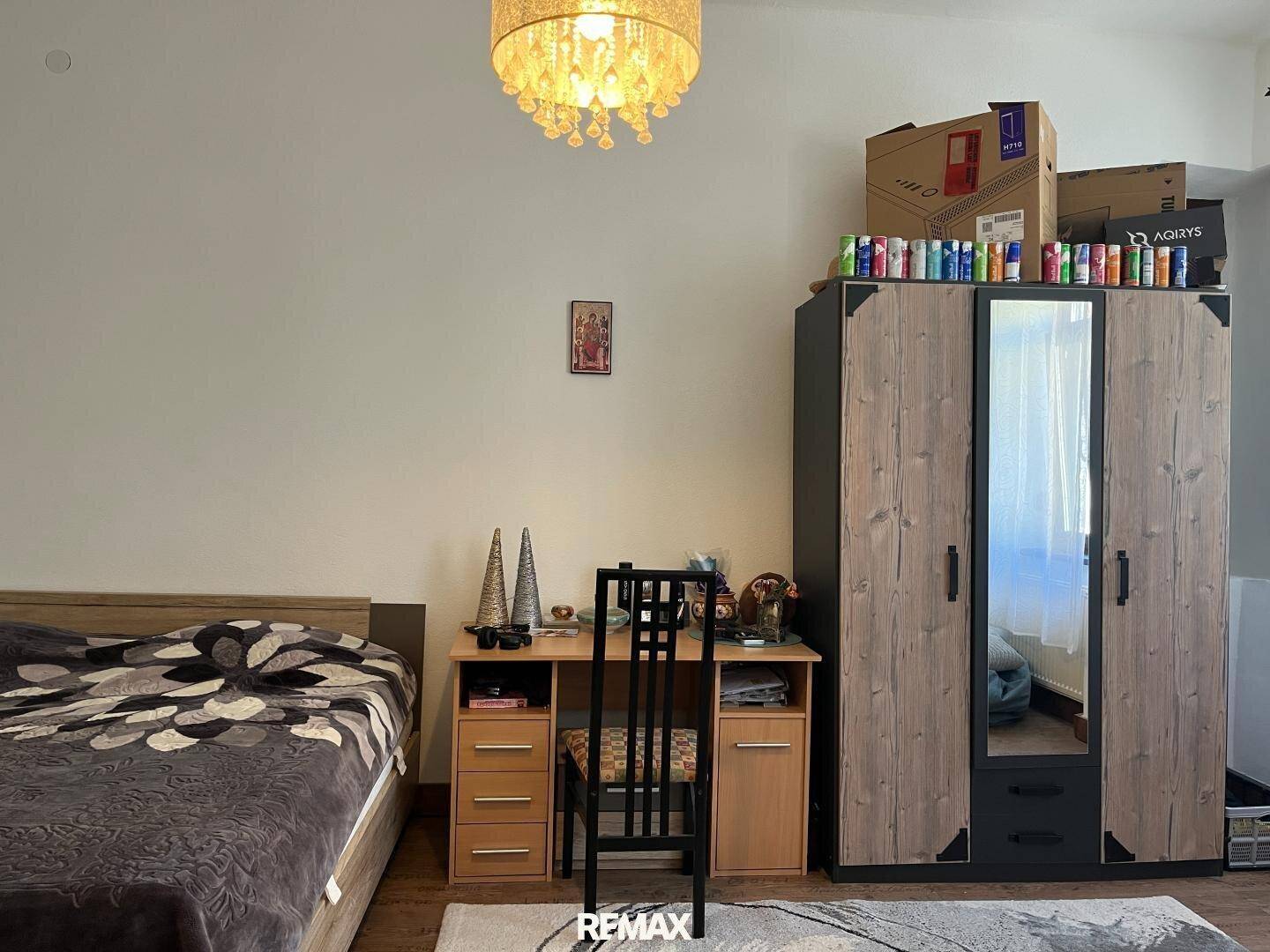 Schlafzimmer mit Bett, Schreibtisch und großem Kleiderschrank mit Spiegel, praktisch eingerichtet.