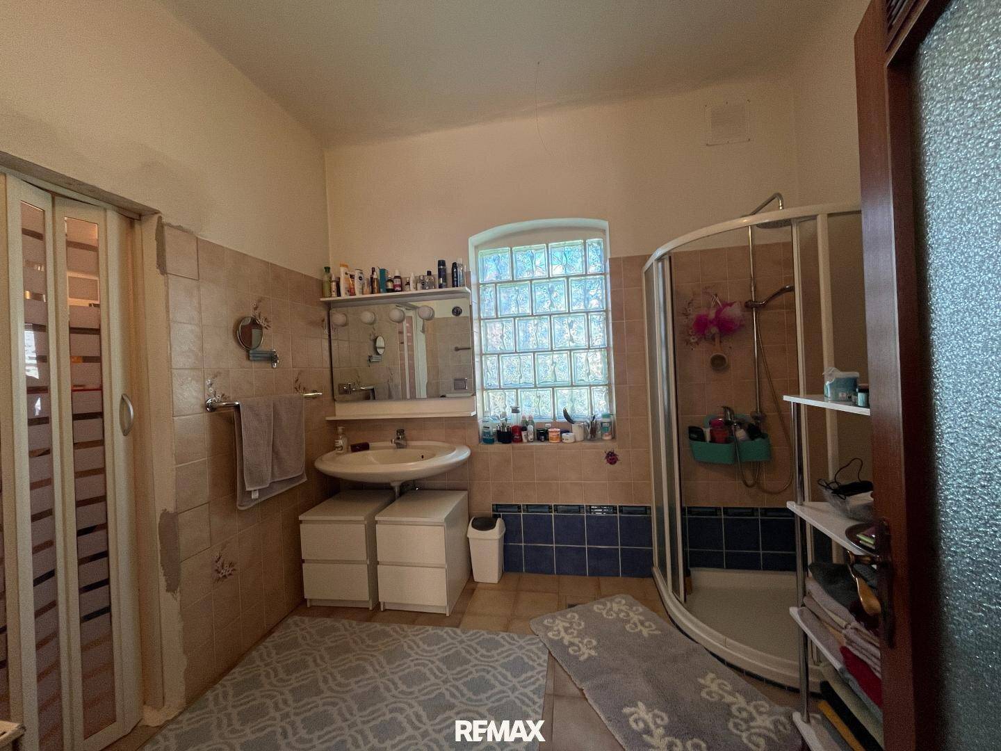 Badezimmer mit Dusche, Waschbecken und Fliesen in Beige- und Blautönen, im Stil der 80er Jahre.