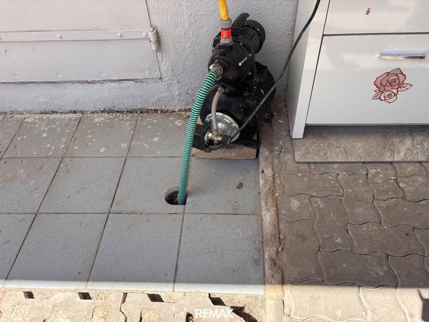 Wasserpumpe mit Schlauch auf gefliestem Boden im Außenbereich, für die Gartenbewässerung.