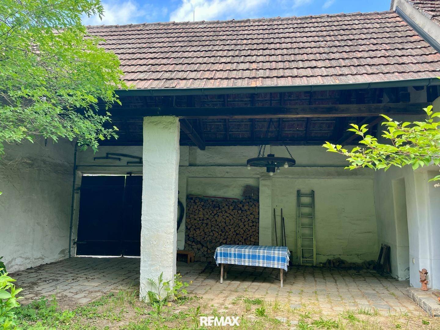Überdachter Außenbereich mit Kopfsteinpflaster, gestapeltem Brennholz und einem rustikalen Holztisch.