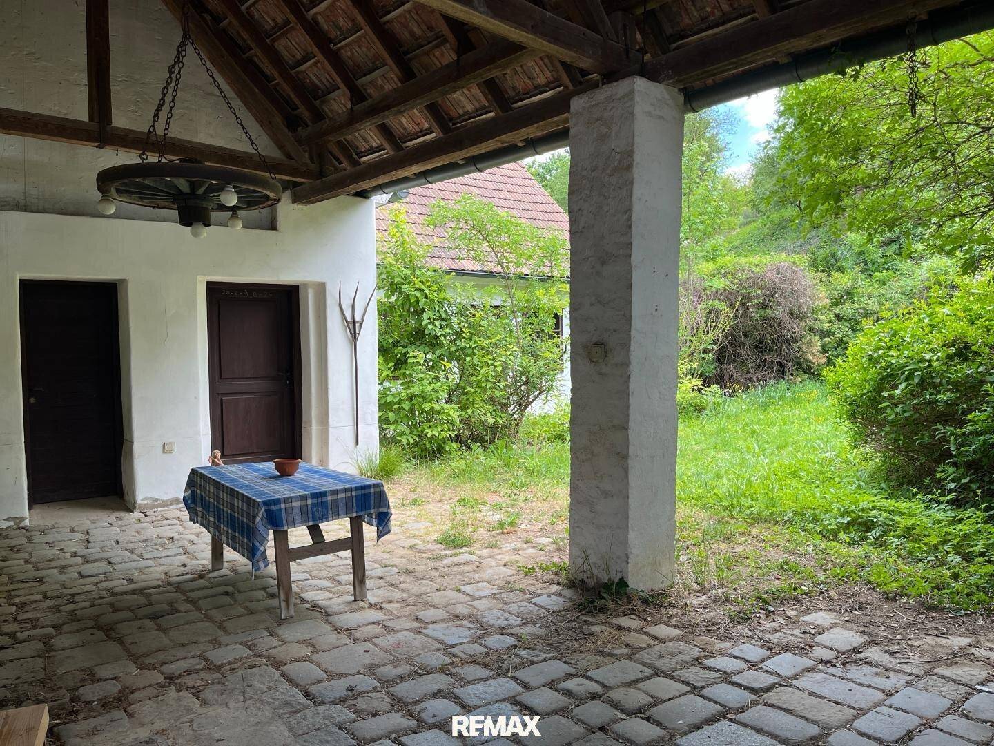 Überdachter Außenbereich mit Kopfsteinpflaster, einer Säule und Blick auf den grünen Garten.