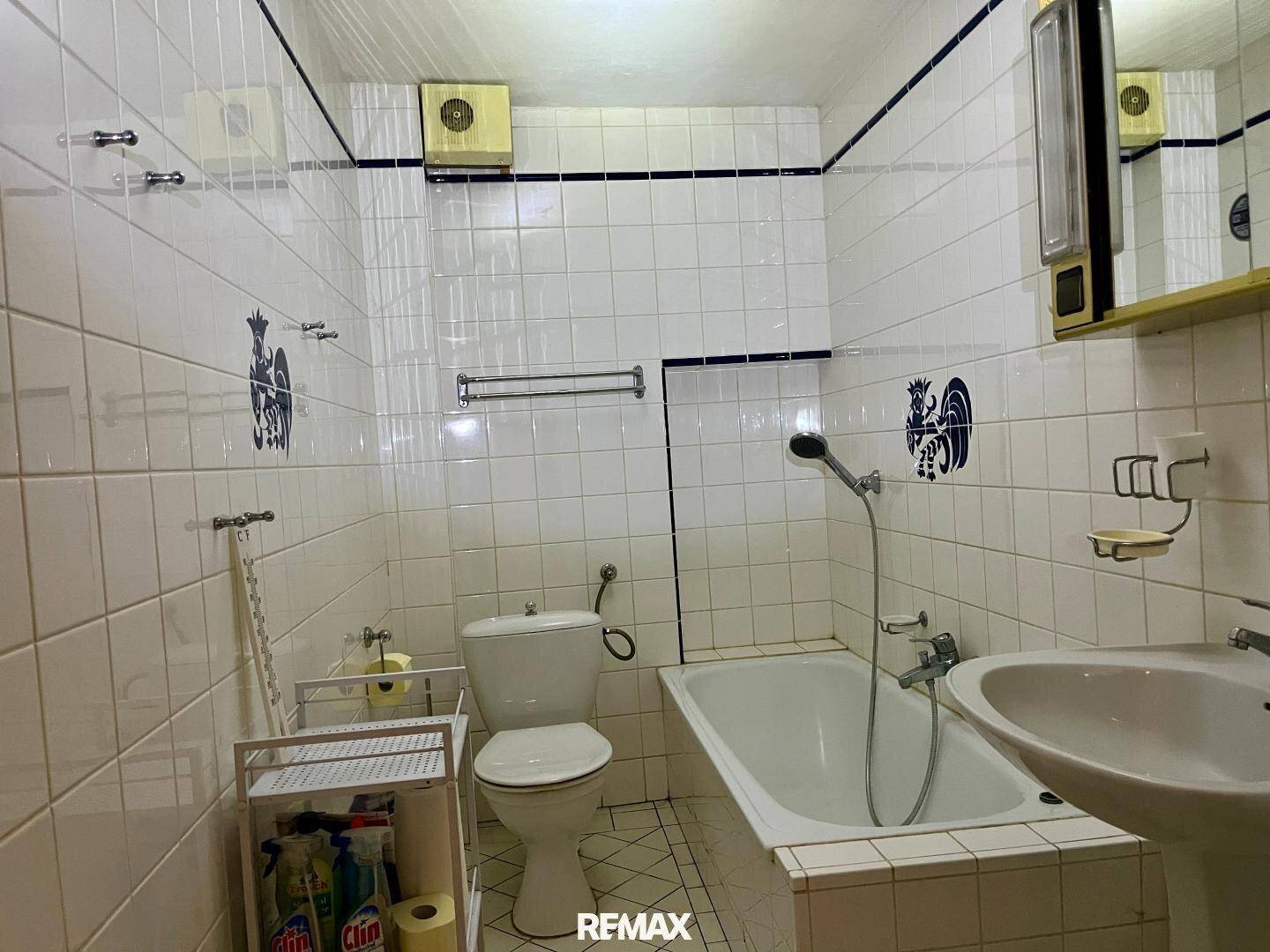 Badezimmer im Stil der 80er Jahre mit weißen Fliesen, blauen Akzenten, Badewanne und Waschbecken.