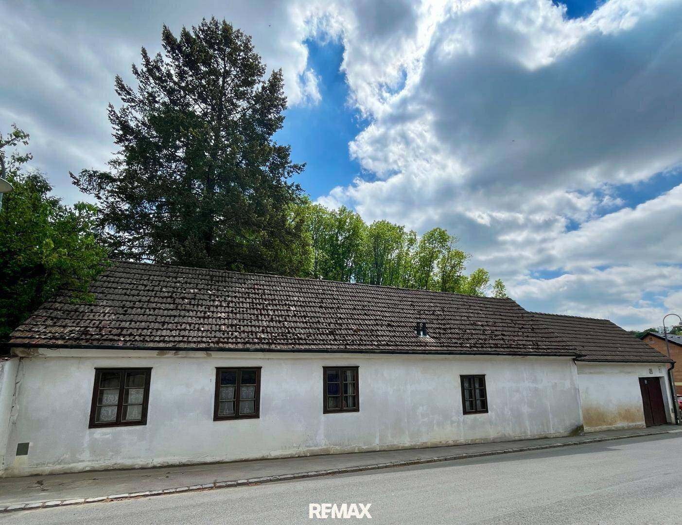 Lange, weiß getünchte Fassade eines traditionellen Landhauses mit braunen Fenstern und Ziegeldach.