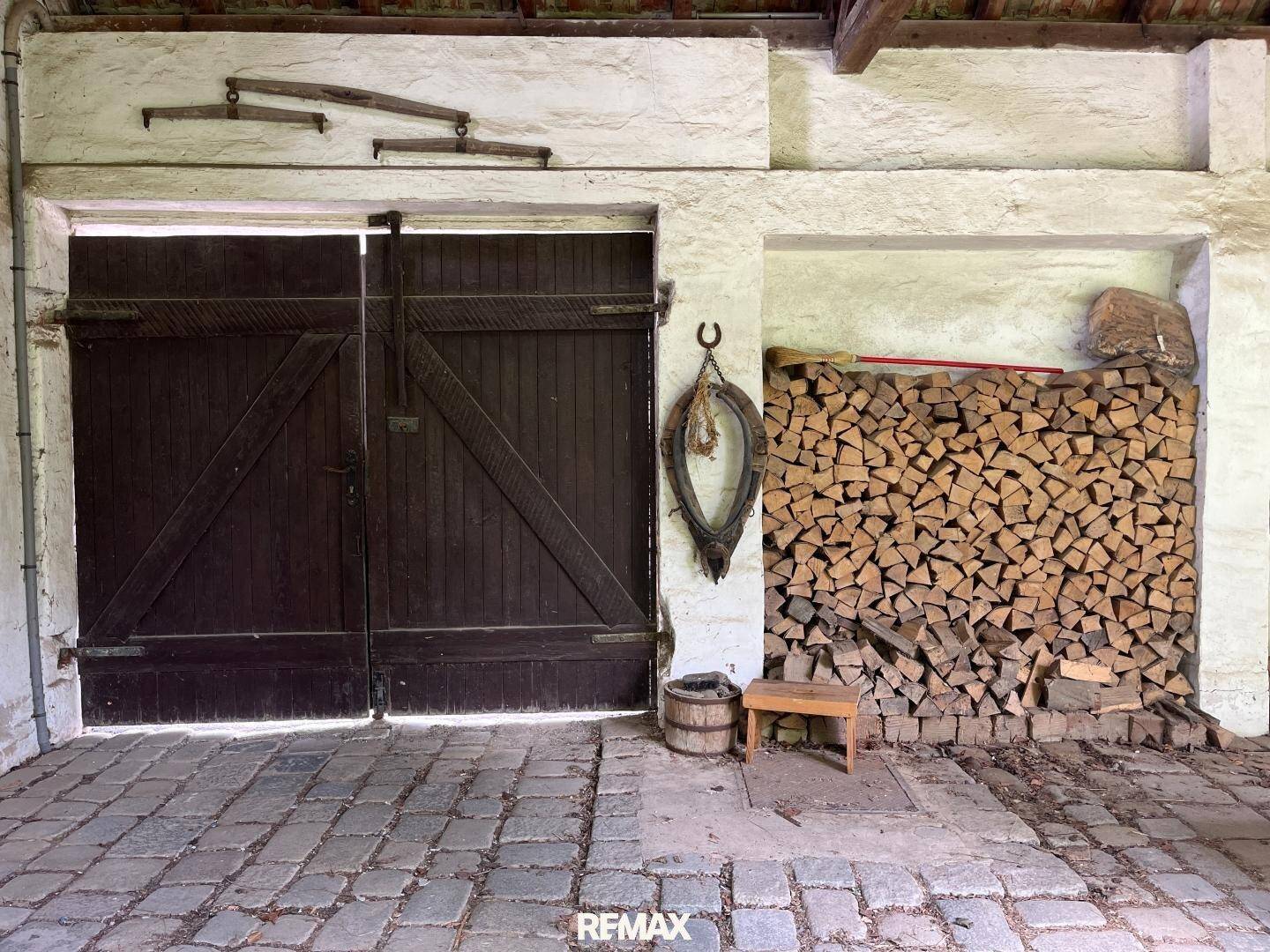 Große Holztüren eines Schuppens oder Stalls mit gestapeltem Brennholz und rustikalen Dekorationen.