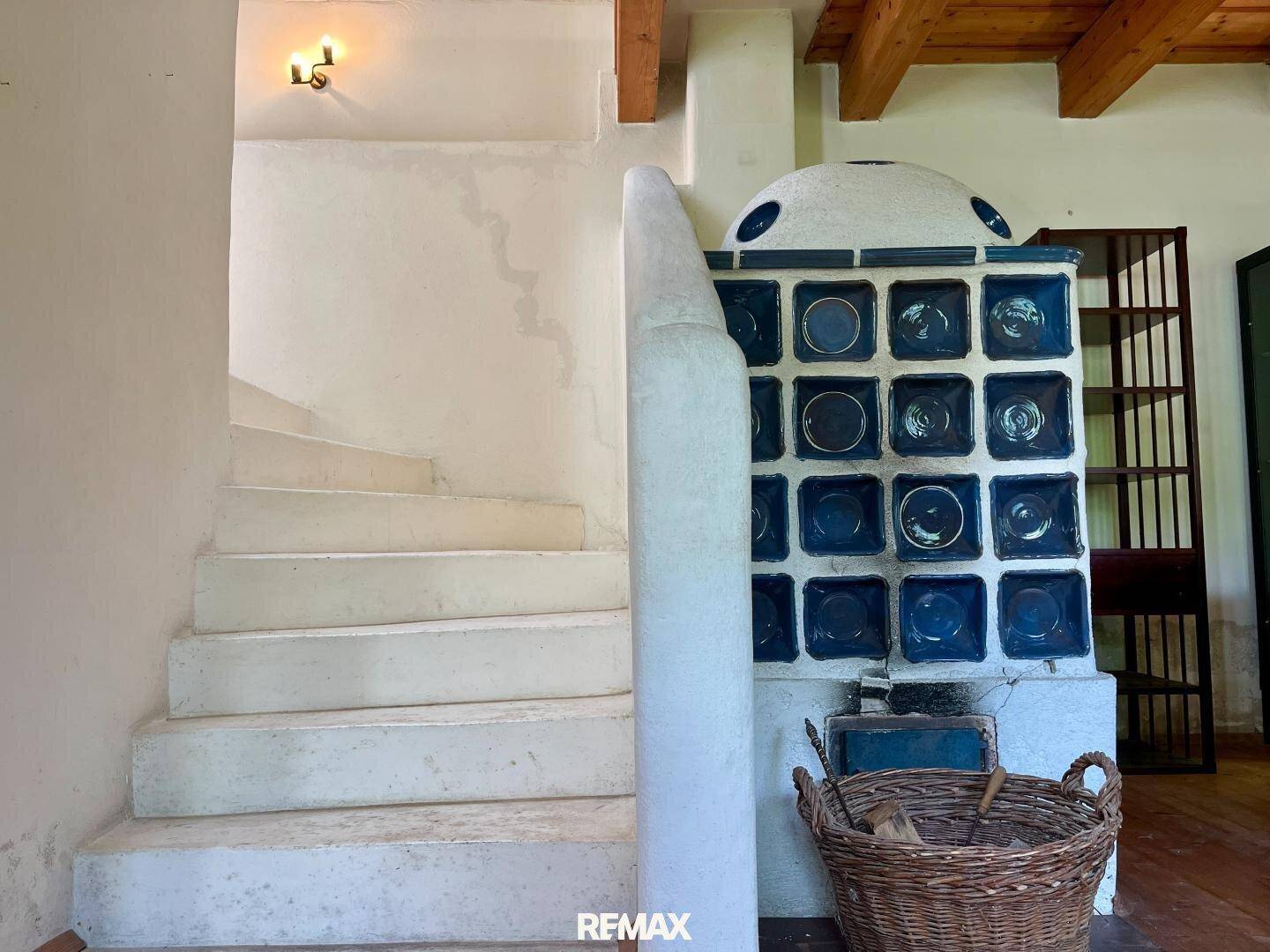 Detailansicht einer weißen Wendeltreppe neben einem traditionellen Kachelofen mit blauen Fliesen.