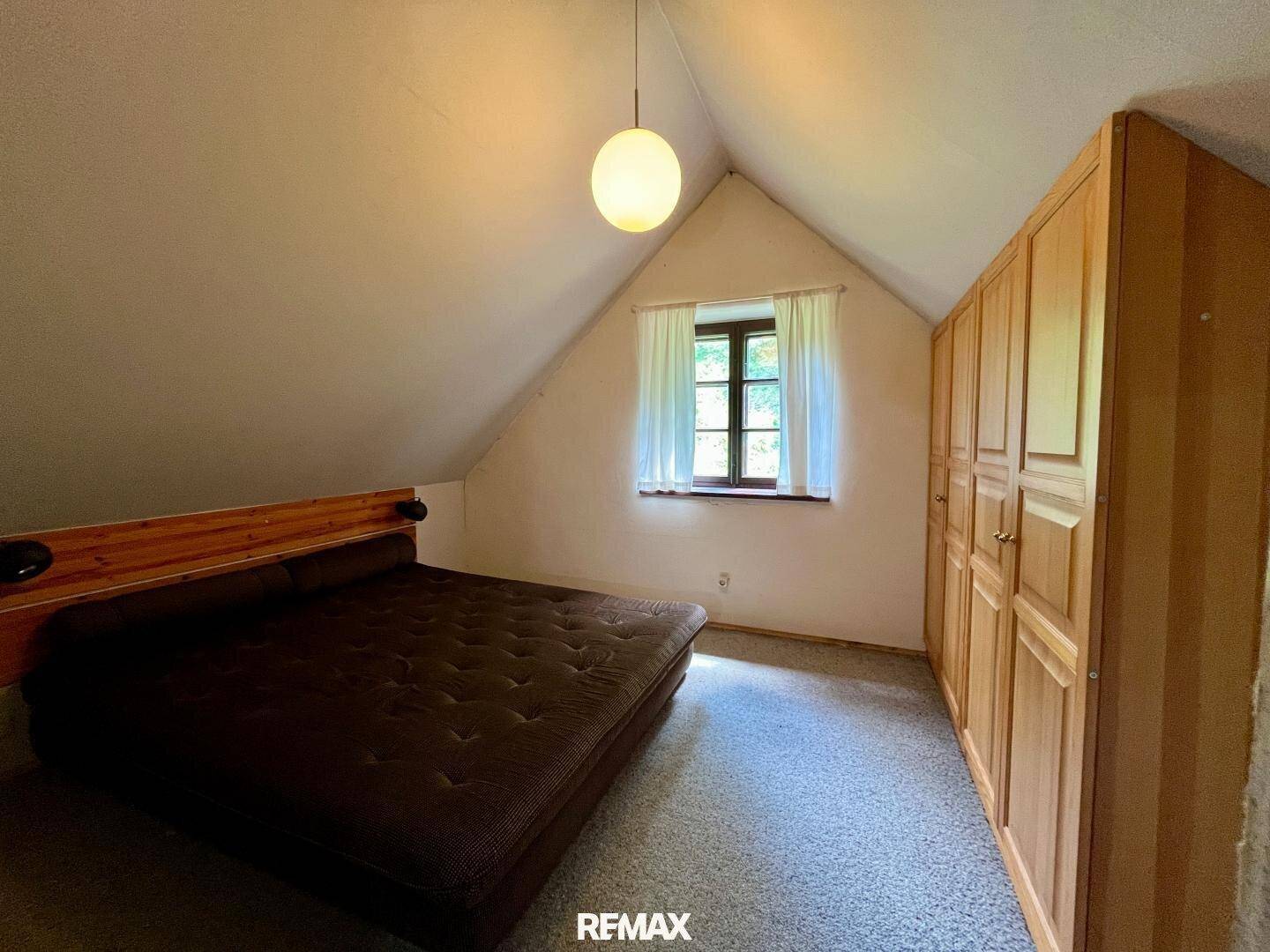 Helles Dachgeschoss-Schlafzimmer mit schrägen Wänden, einem Bett und einem großen Holzschrank.