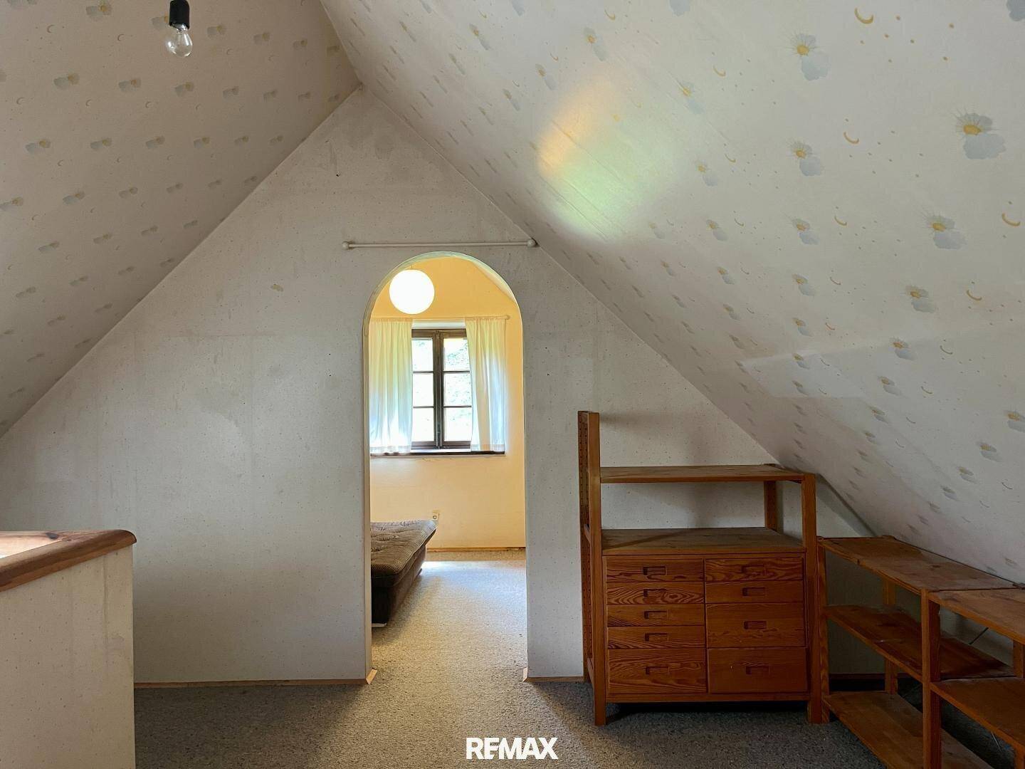 Dachgeschoss-Schlafzimmer mit schrägen Wänden, einem Fenster und einfacher Holzmöblierung.