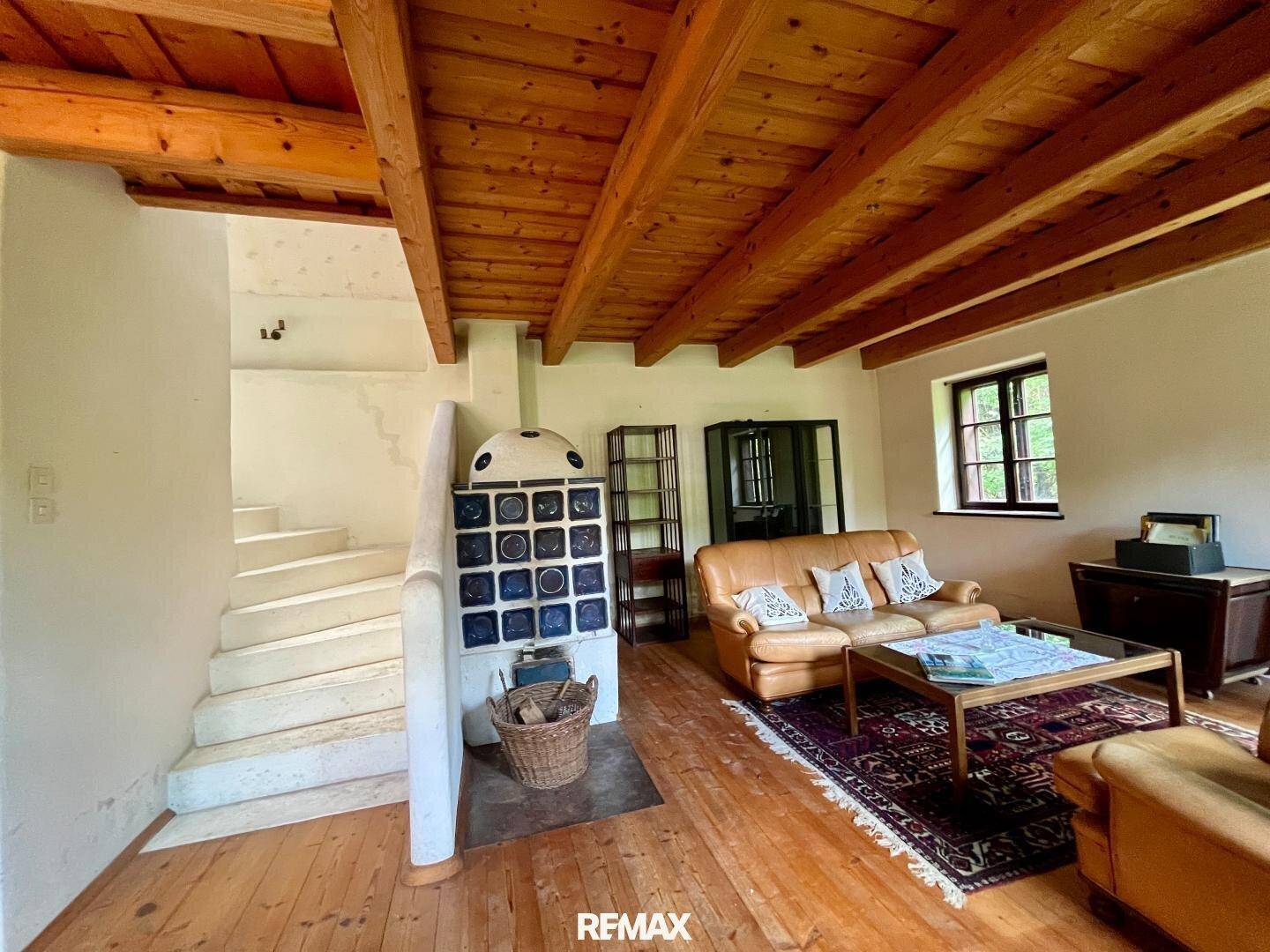 Geräumiges Wohnzimmer mit Holzboden, Ledersofas, Kachelofen und einer Treppe im Hintergrund.
