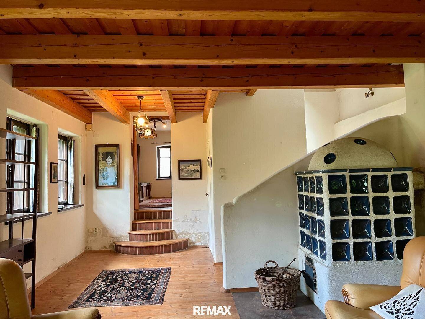 Wohnzimmer mit Holzboden, Kachelofen und einer geschwungenen Treppe, die in die obere Etage führt.