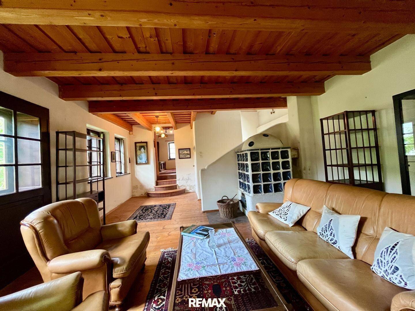Geräumiges Wohnzimmer mit Holzboden, Ledersofas, einem Kachelofen und sichtbaren Holzdeckenbalken.